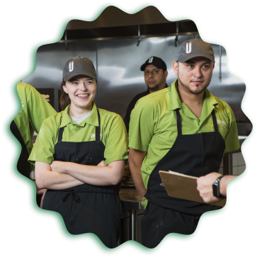 A group of people in green aprons standing next to each other at an Uberrito Mexican restaurant franchise.